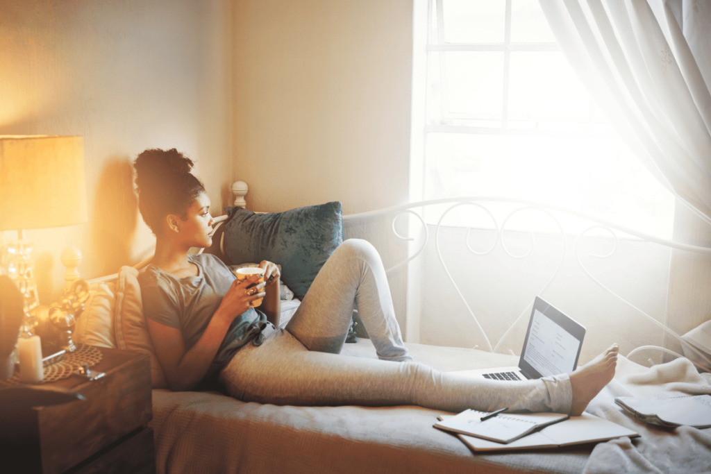 A woman lounges on a bed while holding a cup, taking a break from studying
