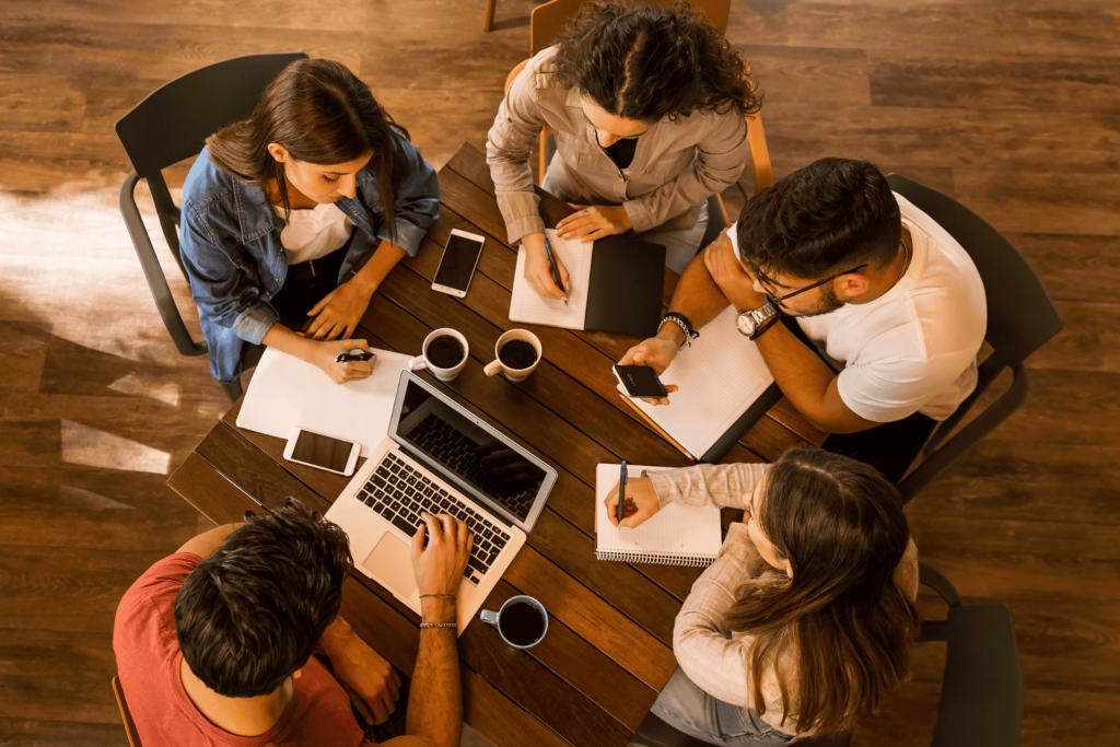  Five people in a study group sitting around a table, studying with notebooks and laptops
